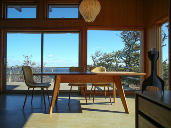The Peter McMahon dining table at the Kohlberg house in Wellfleet has a top of Douglas fir and sculpted ash legs. Blue steel brackets are just visible underneath. Photo courtesy of The Provincetown Independent. Photo by Agata Storer.