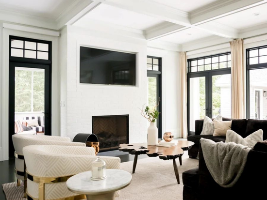 Bright modern living room with white brick fireplace, mounted TV, neutral seating, wood coffee table, and large windows letting in natural light. Taniya Nayak designed this Newton home of Boston Bruins player Patrice Bergeron. Photo Credit: FreeBird Photography.