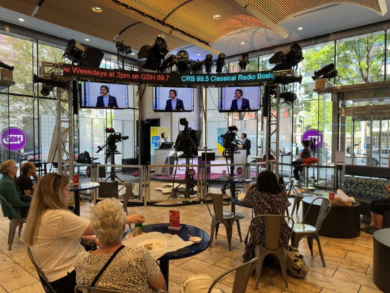 Patrons in the cafe watch as President Mahesh Daas records live with The Culture Show's host Jared Bowen at the GBH's Studio inside Boston Public Library.