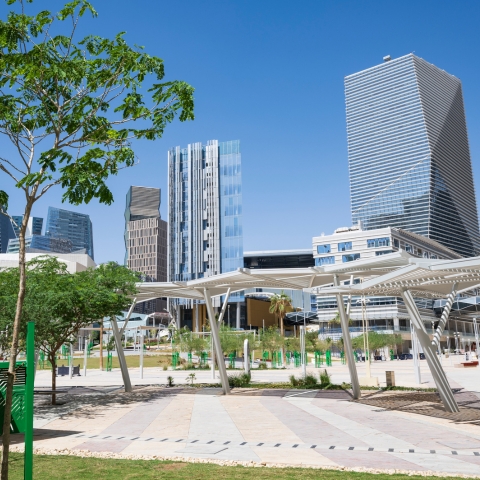 Urban design in action of a modern business district outdoor plaza with geometric paving, shaded walkways, trees, and glass skyscrapers under clear sky.