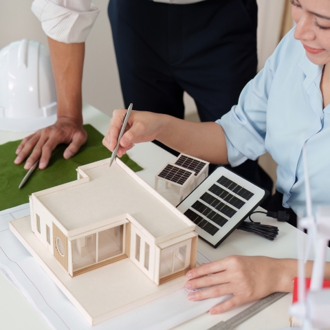 Architect reviewing sustainable house scale model with solar panels during eco-friendly design planning session in introductory studio.