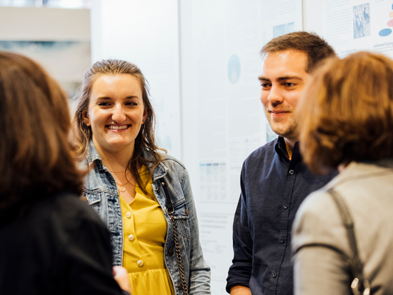 Two people from a group smiling while listening to someone speaking.