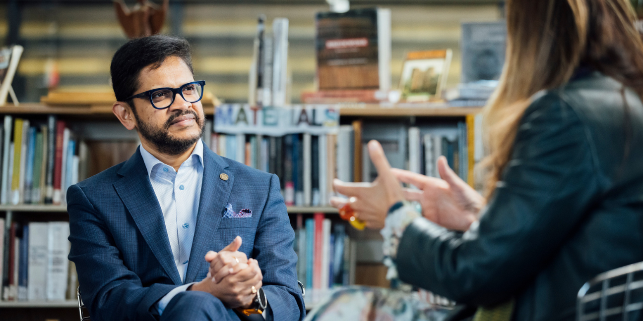 BAC President Mahesh Daas listens intently to Benedetta Tagliabue as she speaks to him during a conversation in the BAC library, with microphones overhead and bookshelves behind them.