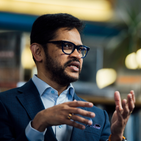 BAC President Mahesh Daas gestures while speaking during a recorded conversation in the BAC library, surrounded by shelves of architecture books.