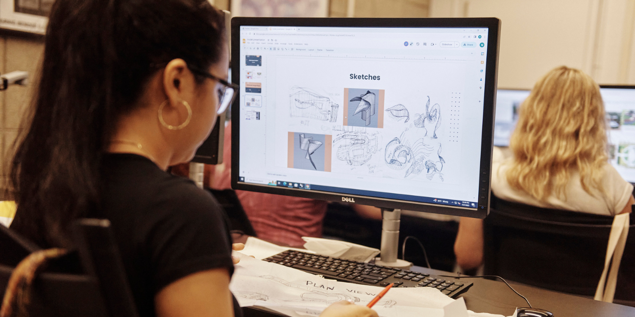 A BAC Summer Academy student works on adding her design sketches to a slideshow on a computer.