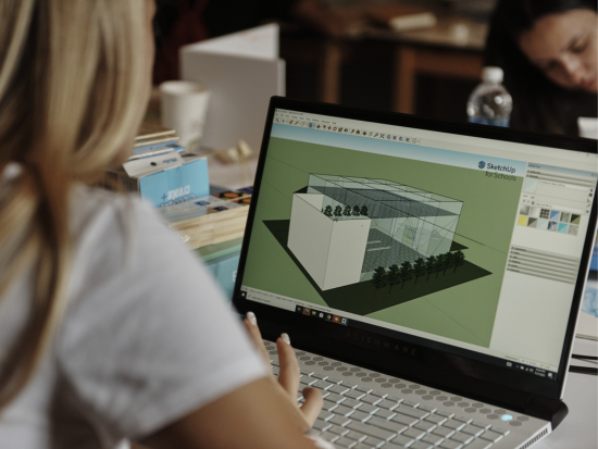 Looking over the shoulder of a BAC Summer Academy student as she works on a building design on a laptop.