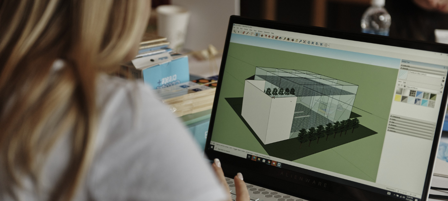 Looking over the shoulder of a BAC Summer Academy student as she works on a building design using Sketch Up for Schools software on a laptop.