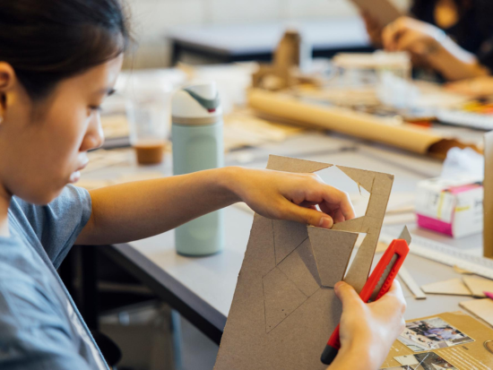 BAC Pre-College Urban Design and Planning Studio student cutting geometric shapes from cardboard with a utility knife while constructing an architectural model in studio.
