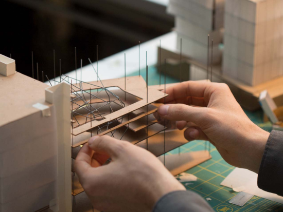 A BAC student's hands carefully work on stablizing the flooring of a building model.
