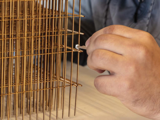 A student carefully adds a stick to a wooden model.