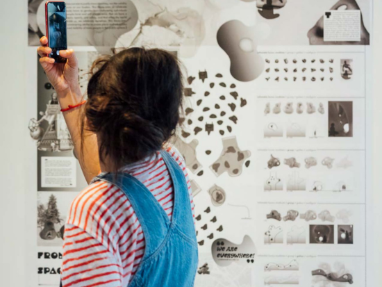 A student takes images of a Graduate Exhibit poster in the BAC's McCormick Gallery.