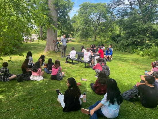 Urban Fellowship Students sit on the grass while listening to a lecture on a field trip.