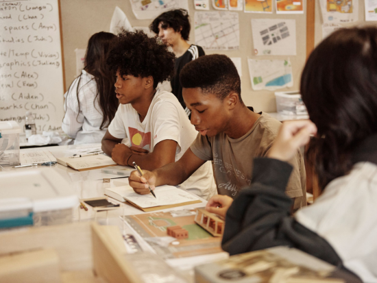 Summer Academy students work on a project in their notebooks and interact.