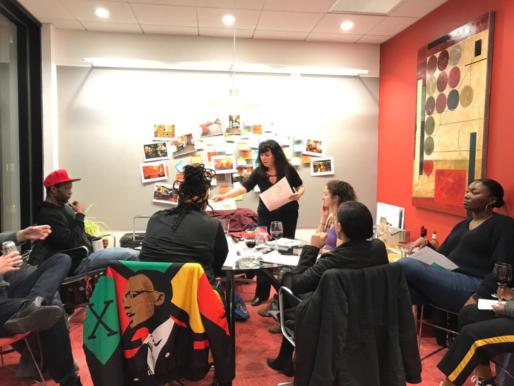 A group of people gather around a table collaborating on designs with photo inspiration on a wall in the background and right side wall.