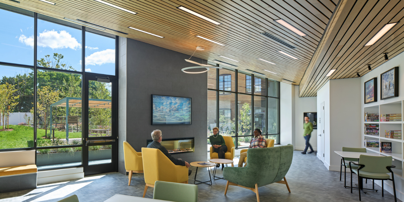 Interior view of The Pryde's new sunroom for residents is designed with a coffee bar, bookcases and a fireplace and large windows overlooking the courtyard. Courtesy of DiMella Shaffer.