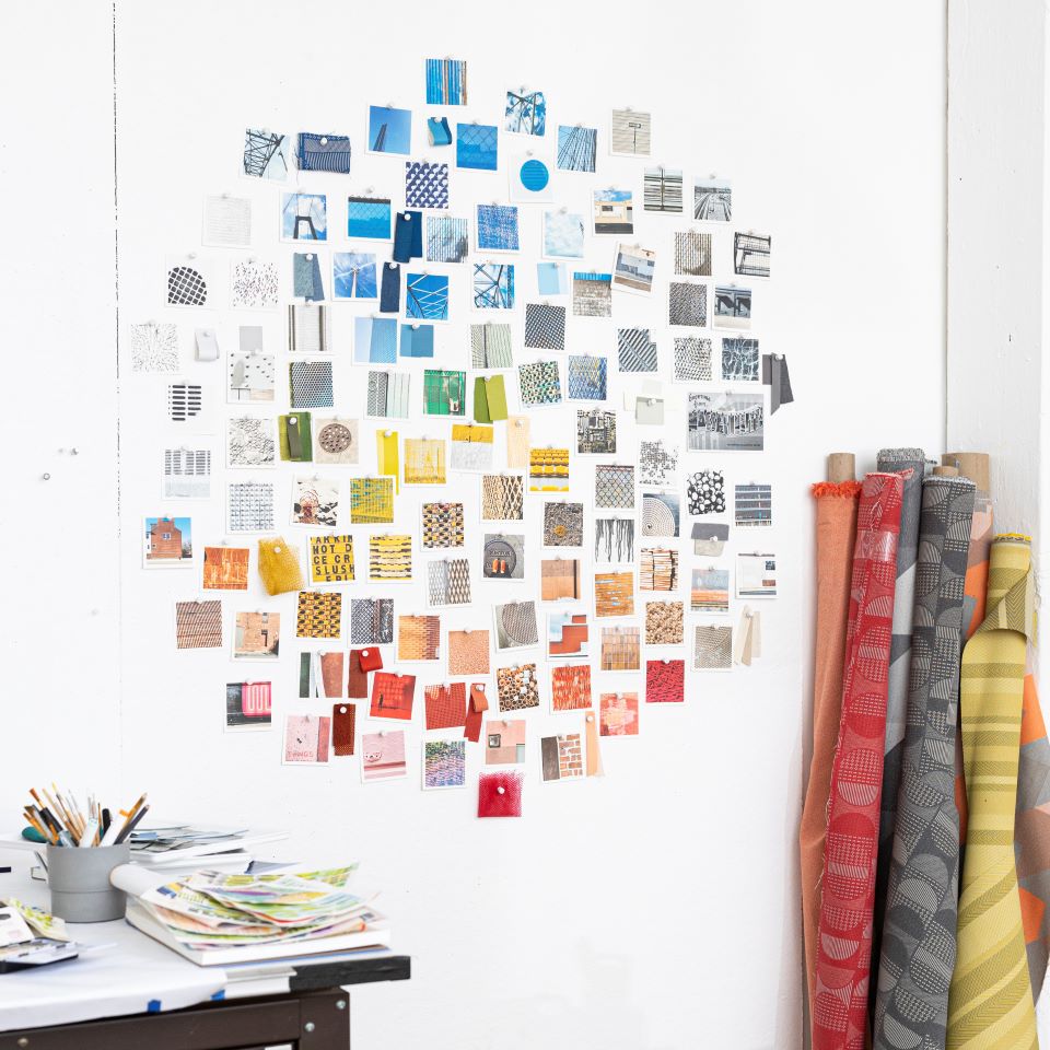 A glimpse inside the design studio of Kelly Harris Smith and the inspiration board that showcases her own photographs paired with textile swatches and paint chips, serving as a reference for patterns, textures, and colors when painting or designing new products.