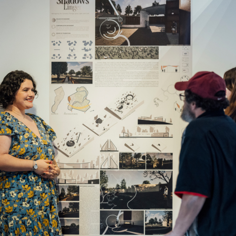 A graduate proudly stands next to her final project board in the 2025 Graduate Exhibit.