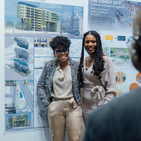 A proud graduate and family member stand in from of the graduate's final project board for a photo at the 2025 Graduate Exhibit.