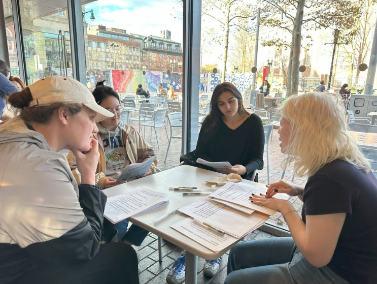 Hannah Wong (right) presenting her work to a group of disabled peers over a table covered in papers. Photo by: Covie Goh.