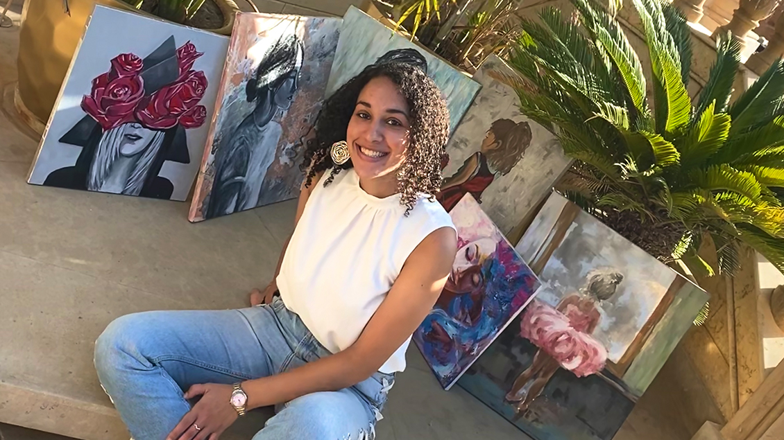 Yasmine sits and poses with some of her paintings in the background