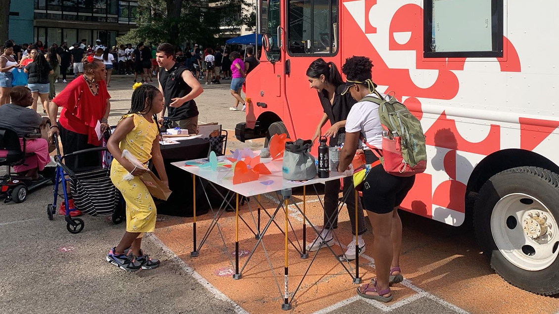 A young girl and elderly woman speaking to volunteers in front of the Mobile Makers Truck