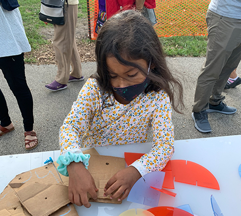 Young girl folding pre-cut cardboard as part of a 3D building project with Mobile Makers