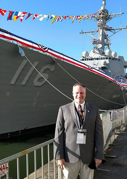 David Wilkins at the USS Hudner Commissioning with the guided-missile destroyer in the background.