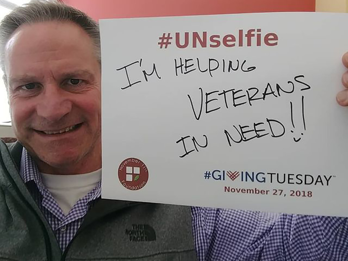 David Wilkins takes his #UNselfie for Giving Tuesday in 2018. The paper he holds states: #UNselfie "I'm helping veterans in need!!" #GivingTuesday November 27, 2018. November 11 Foundation (Logo).