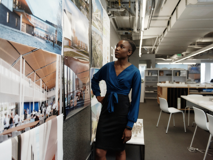 Octavia Pinckney overlooks a wall of posters of building projects at Perkins+Will in Boston. Photo by Tony Luong.