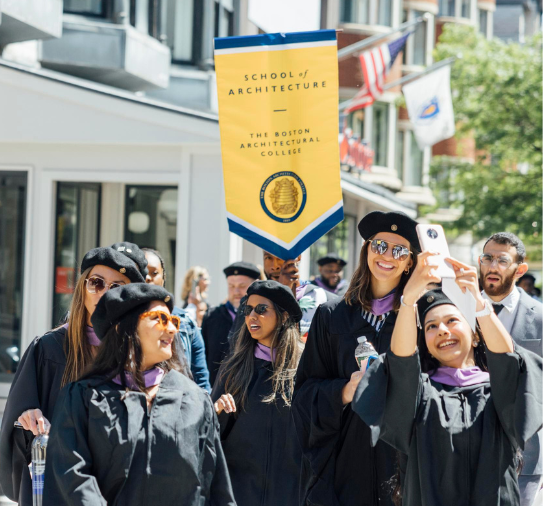 Graduating students walk along with the BAC School of Architecture banner during the promenade to Commencement 2023.
