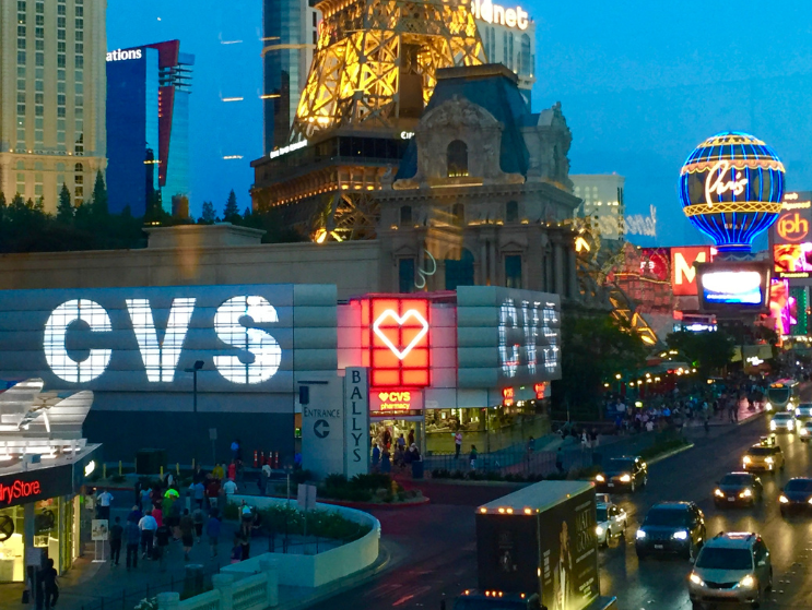 CVS Pharmacy exterior at Bally&rsquo;s Las Vegas at night with neon lights, busy traffic, and the Paris Las Vegas Eiffel Tower in the background.