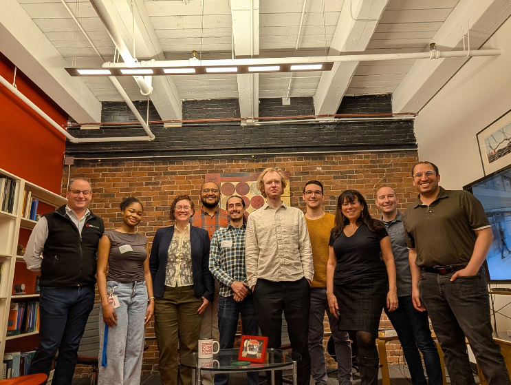 Design professionals, team members, and students pose together in a studio environment.